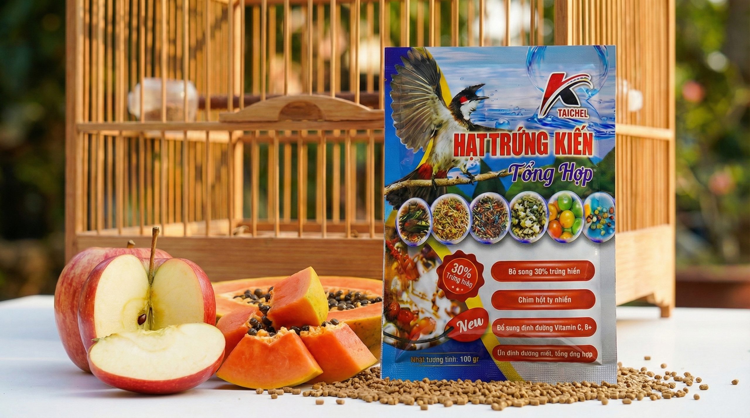 Hình ảnh gói cám Hạt Trứng Kiến Taichel bên cạnh trái cây tươi và lồng lực rộng rãi.